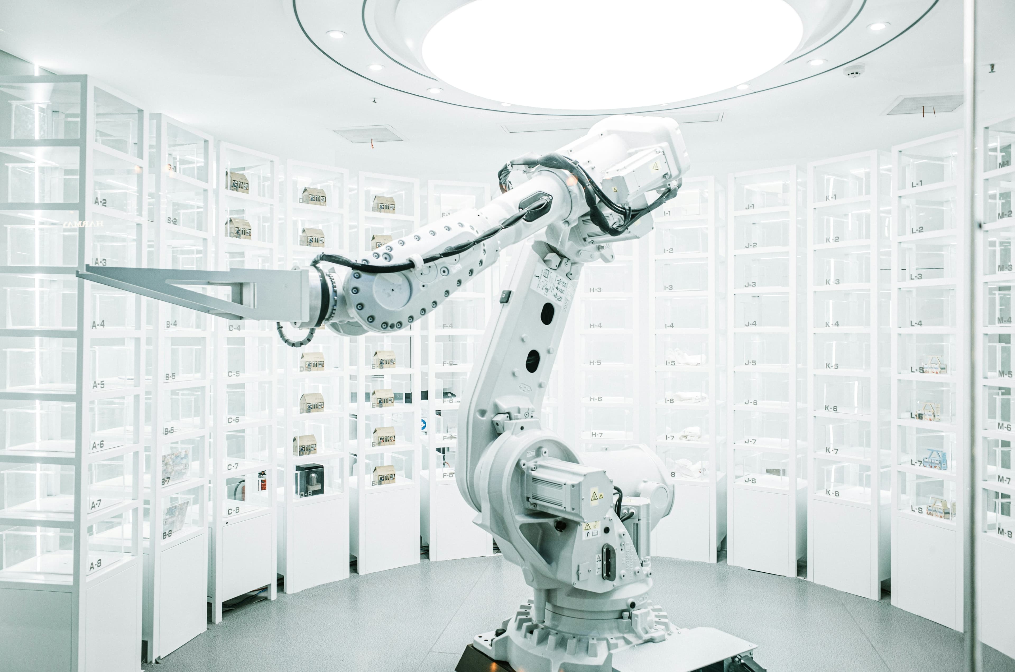 White industrial robot arm in front of rows of labelled storage racks.