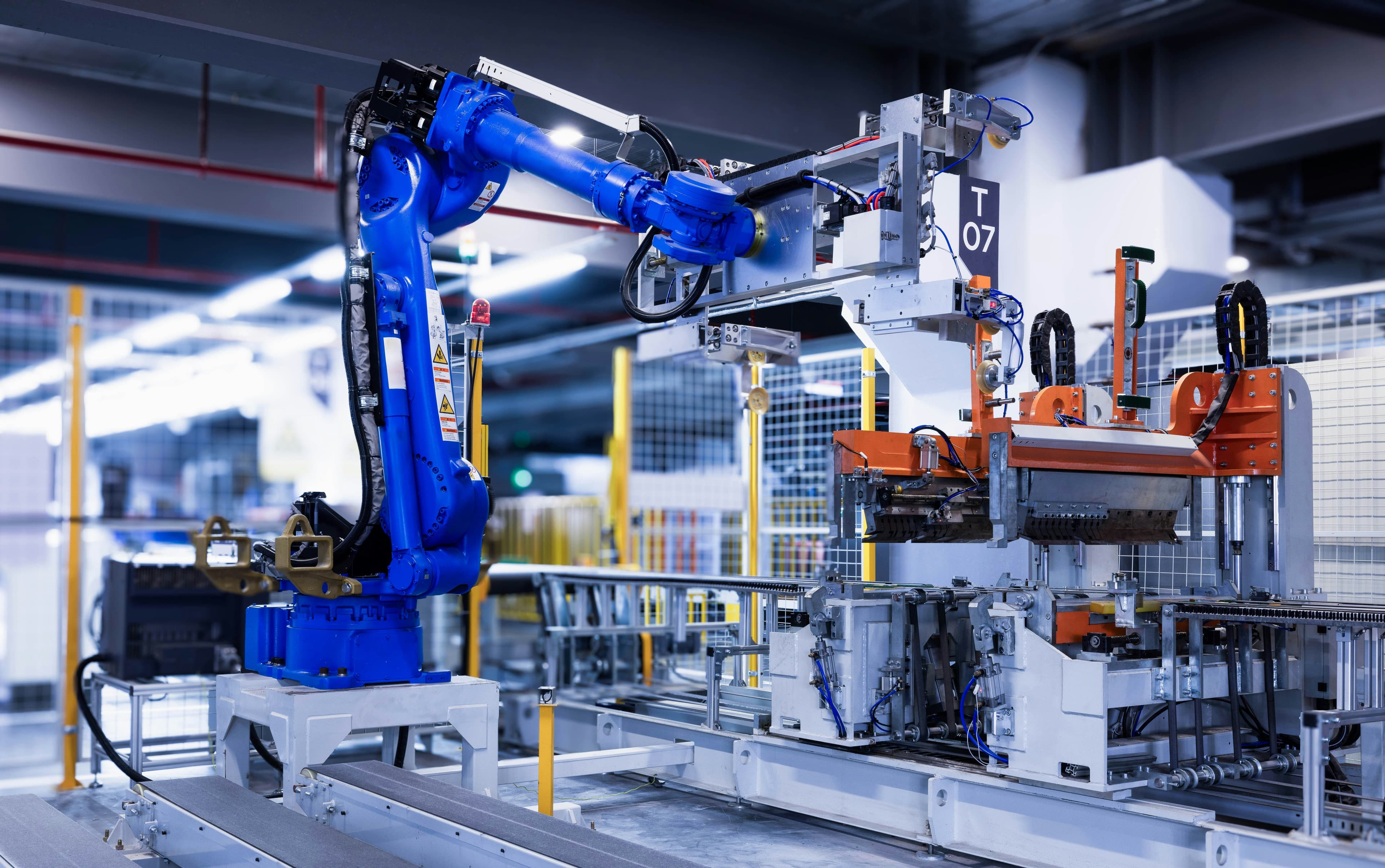 A blue industrial robot arm beside an automated production line in a factory.